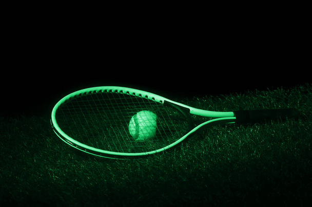 Tennis racket with tennis balls on grass with black background and copy space. Green filter - Photo, Image