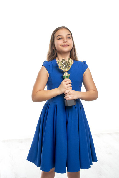 Mavi elbiseli başarılı bir genç kız elinde altın bir kupa, ödüller taşıyor. Beyaz arka planda boynunda madalyalar asılı. Mutlu çocukluk kavramı. - Fotoğraf, Görsel