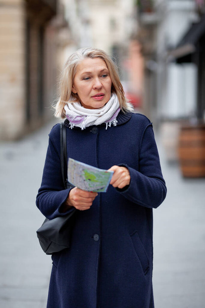 Mulher turista com um mapa na mão caminha ao longo da rua
 - Foto, Imagem