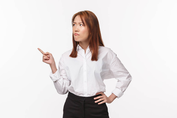 Portrait of skeptical and doubtful young serious-looking asian woman hesitating, pouting and frowning as pointing looking left with disbelief, have doubts, have trust issues, white background - Foto, afbeelding