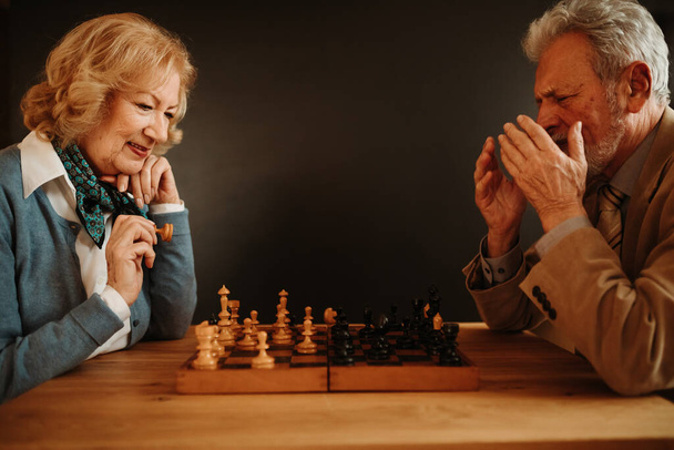 自宅でチェスをしている高齢者のカップルの近い写真。女が勝つから男は幸せじゃない. - 写真・画像
