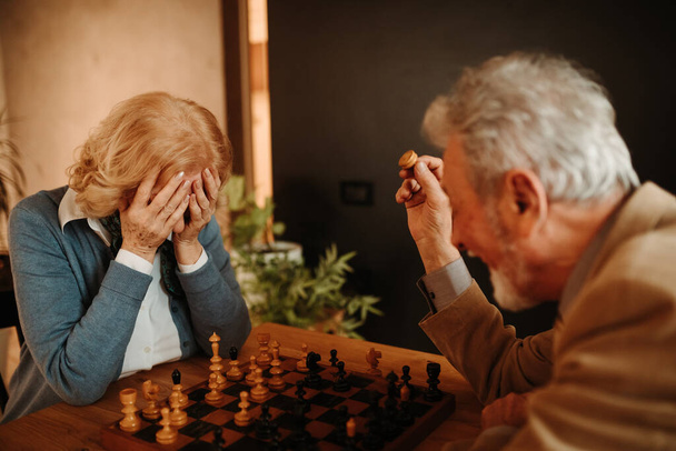 Portrait of blonde woman feeling blue because her husband is winning in chess game at home. - Photo, Image