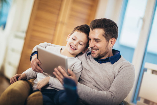 Vader en zoon spelen op een tablet thuis, plezier - Foto, afbeelding