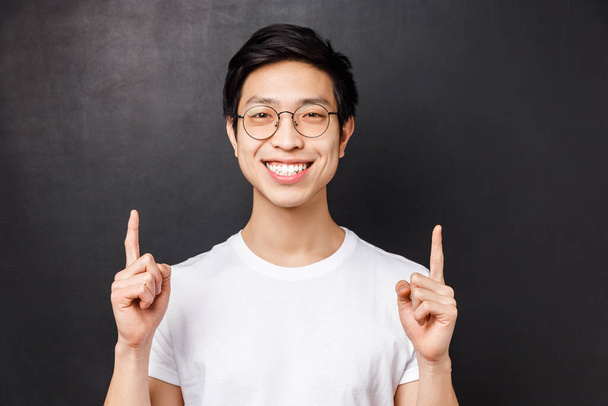 Κοντινό πλάνο πορτρέτο ενός χαρούμενου, χαρούμενου Ασιάτη νεαρού φοιτητή που μιλάει για την εμπειρία του από σπουδές στο εξωτερικό, δείχνοντας τα δάχτυλά του στην παρουσίαση, χαμογελώντας ικανοποιημένος και ξέγνοιαστος - Φωτογραφία, εικόνα