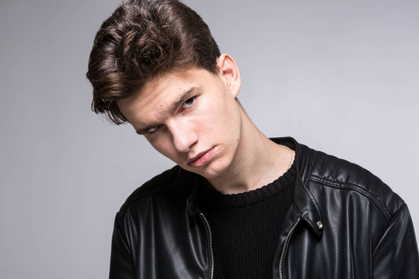 Wide angle. Studio shot. Young caucasian guy model in black clothes posing in the studio. Teenager in Leather Jacket Standing Against White Background. young fashion model wearing black coat in studio - 写真・画像
