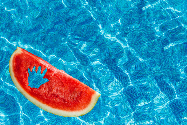 У басейні з блакитною водою шматочок кавуна з різьбленим дитячим ручним плаванням. Копіювати простір. Вид зверху
. - Фото, зображення