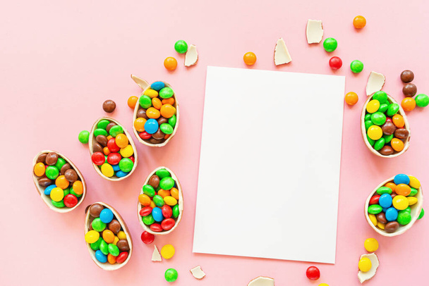 Chocolate Easter eggs, blank of paper and colorful candies on pastel pink paper background. flat lay, copy space, top view, overhead, template, mockup. - Photo, image