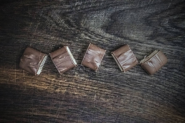 Una barra de chocolate cortada en pedazos se encuentra sobre un fondo de madera oscura. Copiar espacio, plano laico
. - Foto, imagen