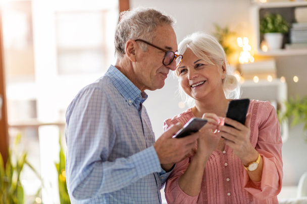 Couple âgé regardant un smartphone ensemble à la maison
 - Photo, image