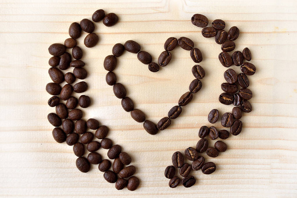 Coffee beans spilled on wooden board grouped into heart shape. - Photo, Image