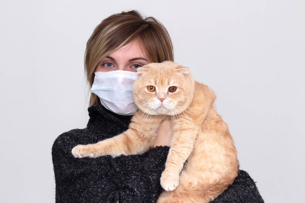 Cute girl with a cat, wearing a health mask, isolated in the background, flu epidemic, dust Allergy, virus protection. Concept of air pollution in the city, close- up - Φωτογραφία, εικόνα