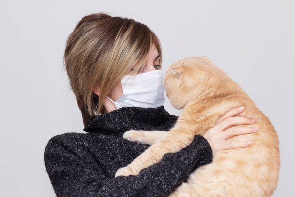 Cute girl with a cat, wearing a health mask, isolated in the background, flu epidemic, dust Allergy, virus protection. Concept of air pollution in the city, close- up - Photo, image