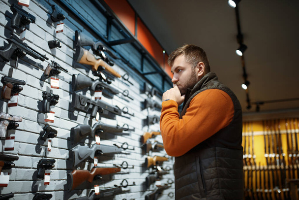 Man looking on handguns on showcase in gun shop. Euqipment for hunters on stand in weapon store, hunting and sport shooting hobby  - Φωτογραφία, εικόνα