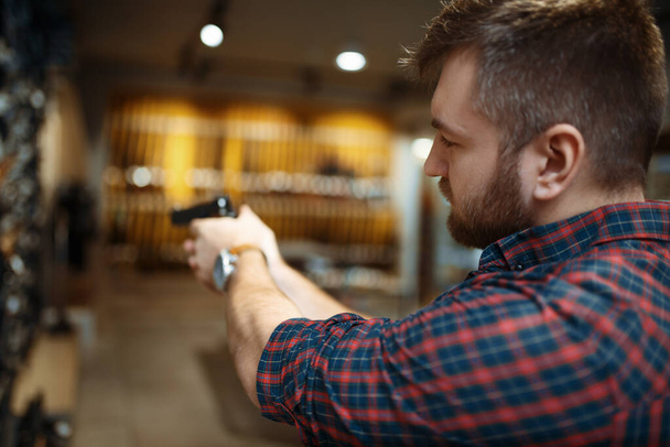 Mann zielt mit neuer Handfeuerwaffe auf Waffengeschäft Männliche Person kauft Pistole zur Sicherheit im Waffengeschäft, Selbstverteidigung und Sportschießen Hobby - Foto, Bild
