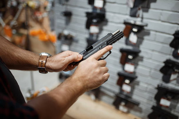 Man choosing new handgun at showcase in gun shop. Male person buying pistol for security in weapon store, selfdefence and sport shooting hobby - Fotografie, Obrázek