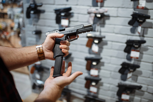 Man choosing new handgun at showcase in gun shop. Male person buying pistol for security in weapon store, selfdefence and sport shooting hobby - Foto, Imagen