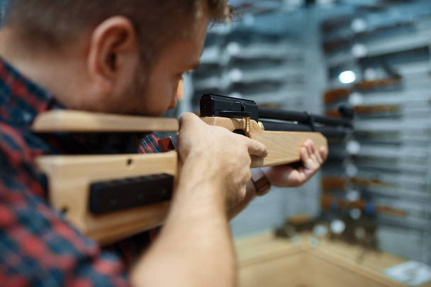 Mężczyzna ze strzelbą pneumatyczną na wystawie w sklepie z bronią. Euqipment dla myśliwych na stoisku w sklepie z bronią, myślistwo i strzelanie sportowe hobby - Zdjęcie, obraz