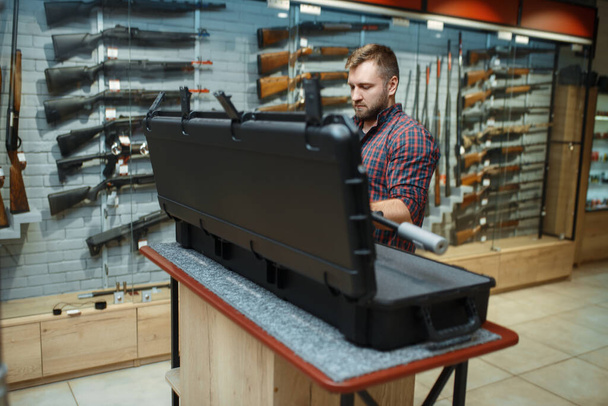 Man takes sniper rifle from the case in gun shop. Euqipment for hunters on stand in weapon store, hunting and sport shooting hobby - Photo, Image
