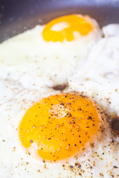 Fried egg close-up: whole yolk in focus. The concept of fried food, breakfast. Egg sprinkled with pepper. - Fotografie, Obrázek