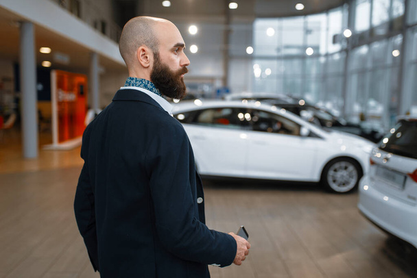 Hymyilevä mies poseeraa autokaupassa. Asiakas uuden auton näyttelytilassa, mies ostaa auton, auto jälleenmyyjä liiketoimintaa
 - Valokuva, kuva