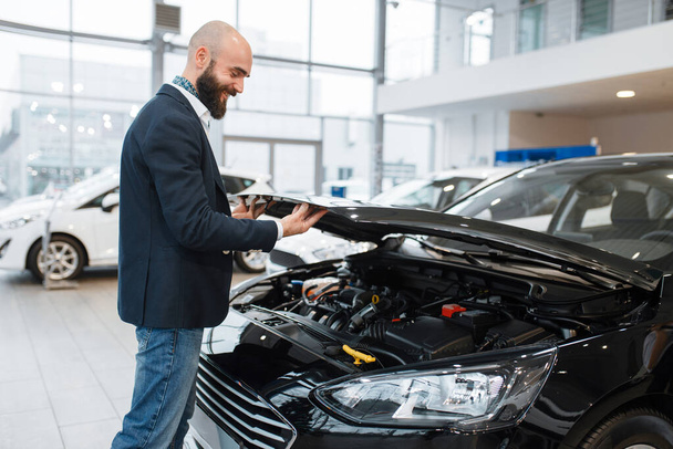Man looking on transport engine in car dealership. Customer in new vehicle showroom, male person buying automobile, auto dealer business - Photo, image