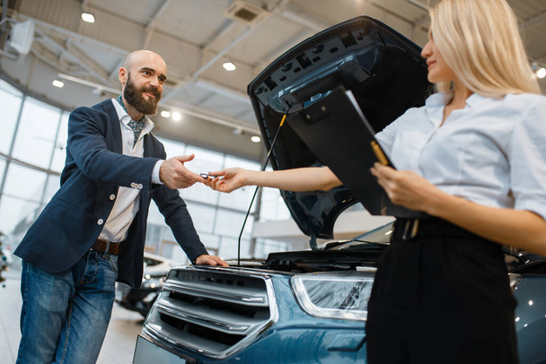Adam ve satıcı kız araba galerisinde araba seçiyor. Araç galerisinde müşteri ve satıcı, ulaşım satın alan erkek, otomobil satıcısı - Fotoğraf, Görsel