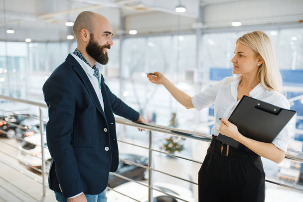 Female seller invites man to presentation in car dealership. Customer and saleswoman in vehicle showroom, male person buying transport, automobile dealer business - Zdjęcie, obraz