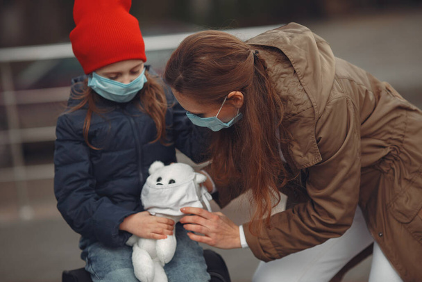 A European mother in a respirator with her daughter are standing near a building.The parent is teaching her child how to wear protective mask to save herself from virus - Foto, imagen