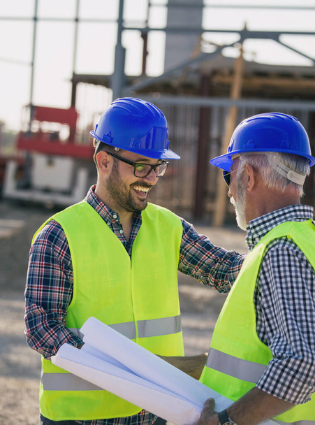 Zwei Ingenieure beim Händeschütteln auf einer Baustelle mit Metallkonstruktion im Hintergrund - Foto, Bild