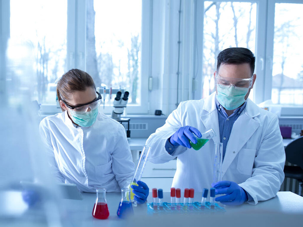 Laboratuvarda cam şişelerde bazı kimyasalları test eden iki biyolog. - Fotoğraf, Görsel