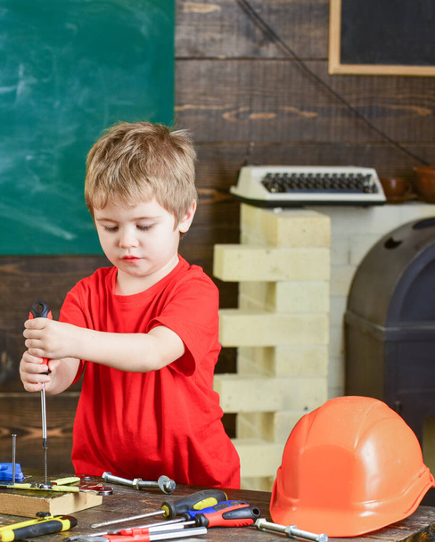 Концентрированный ребенок привязывает винт к деревянной доске обеими руками. Блондин работает в ремонтной мастерской. Дошкольник приобретает новые навыки
 - Фото, изображение