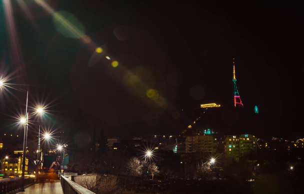 Saarbrucken bridge and Tbilisi broadcasting tower at night illuminated by traditional lithuanian flag colors: yellow, green , red. 11th of march, Lithuania's independence day. Tbiliso.Sakartvelo. Georgia.11.03.2020 - Photo, Image