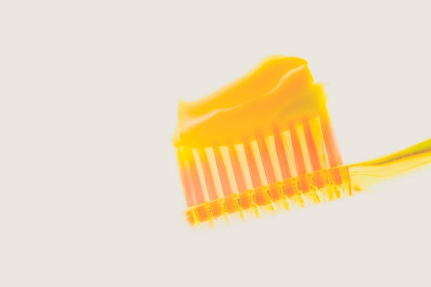 Yellow plastic toothbrush with melon toothpaste on an isolated background. Side view - Photo, Image