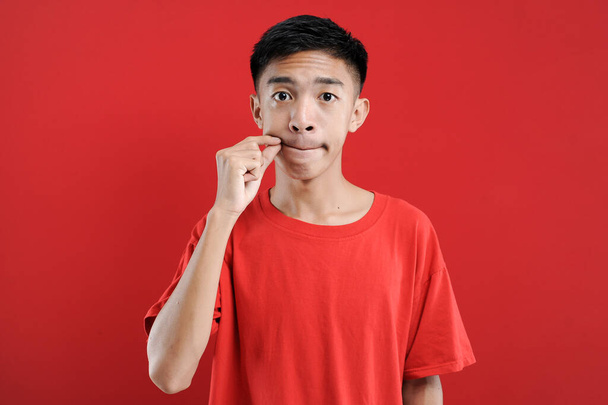 Ázsiai jóképű férfi csinál néma gesztus elszigetelt piros háttér nézi a kamera - Fotó, kép