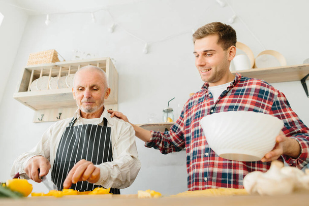 Nuori mies ja hänen isänsä ruoanlaitto keittiössä
 - Valokuva, kuva