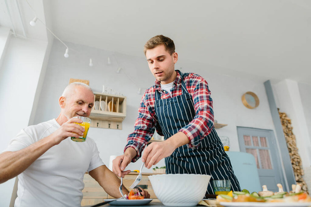 Молодий чоловік і його батько готують на кухні
 - Фото, зображення
