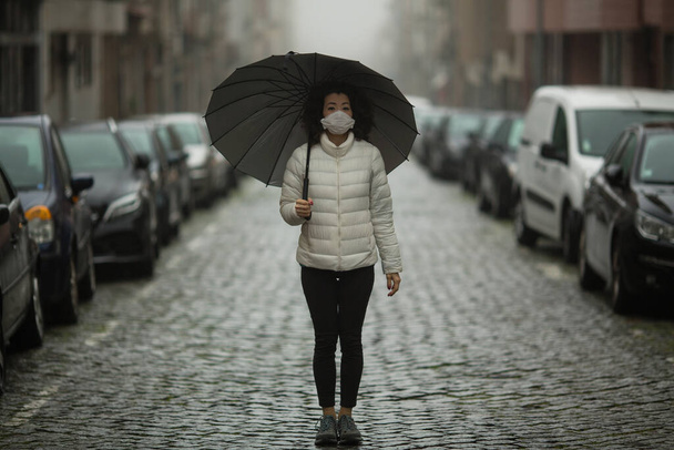 Пандемія. Багатокультурна азіатка в антивірусній масці стоїть на вулиці в похмуру погоду
. - Фото, зображення