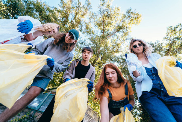 Un groupe d'amis militants jettent beaucoup d'ordures dans un sac. Tir du bas vers le haut
 - Photo, image