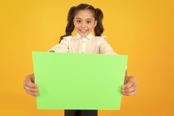 Being given a home work. Little child holding empty sheet for examination work on yellow background. Small girl with blank green paper for project work or research. Paper work, copy space - Foto, Bild