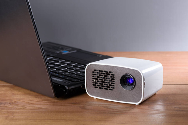 Battery-powered mini projector with a notebook on a desk. The image is transmitted wirelessly. - Valokuva, kuva