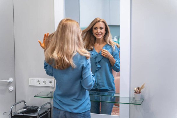 Positive delighted young blonde looking at her reflection - Fotoğraf, Görsel