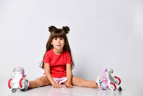 Beautiful girl posing sitting on the floor, in a red t-shirt and shorts and a fashionable hairstyle, in roller skates on her feet - Photo, image