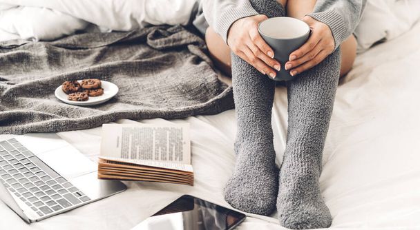 Молода жінка розслабляється і п'є чашку гарячої кави або чаю в холодний зимовий день у спальні
 - Фото, зображення