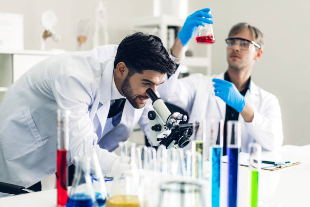 Επαγγελματίας δύο επιστήμονας άνθρωπος κάνει ένα χημικό πείραμα, ενώ κάνοντας μια έρευνα και χρησιμοποιώντας μικροσκόπιο με ανάμειξη χημικών ουσιών σε δοκιμαστικό σωλήνα στο σύγχρονο Εργαστήριο - Φωτογραφία, εικόνα