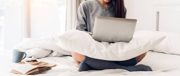 Молода жінка розслабляється за допомогою портативного комп'ютера в холодний зимовий день в спальні.жінка перевіряє соціальні додатки і працює.
 - Фото, зображення
