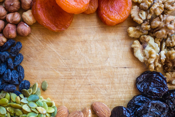 Dried apricots, raisins, hazelnuts, walnuts, pumpkin seeds and almonds are lined with a frame. In the center is an old, vintage surface made of wood. Warm colors, natural light. - Photo, Image