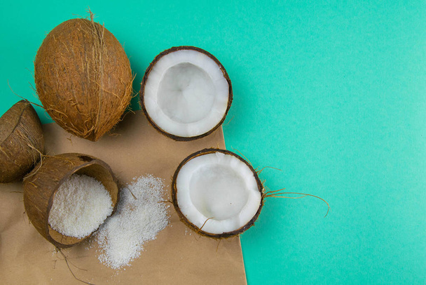 Gebroken kokosnoten op papier die op een turquoise ondergrond staat, naast verspreid kokosschaafsel. - Foto, afbeelding