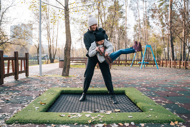 Annesi ve kızı sonbahar parkında trambolinde birlikte zıplıyorlar. - Fotoğraf, Görsel