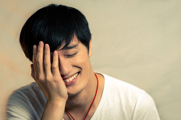 νεαρός άνδρας, που καλύπτουν το πρόσωπό του και να χαμογελά - Φωτογραφία, εικόνα
