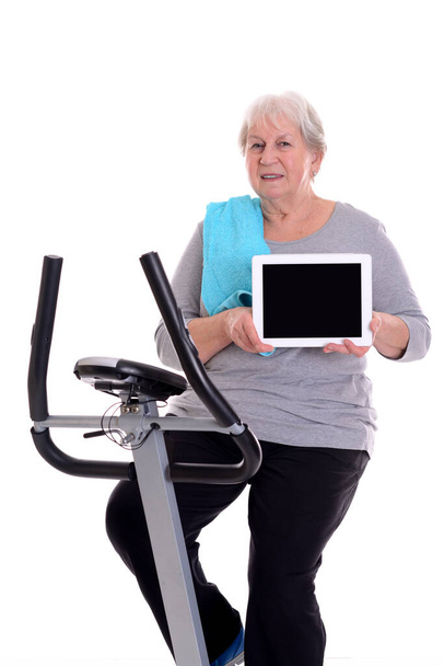 gray-haired female senior train with fitness machine and showing tablet PC - Foto, Imagem